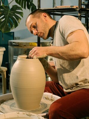 An artisan focuses on shaping clay pottery with precision in a well-lit studio.