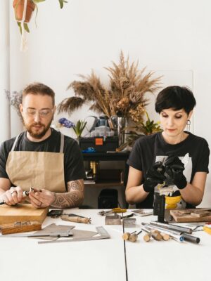 Two artisans creating jewelry with precision and creativity in a modern, plant-adorned studio.